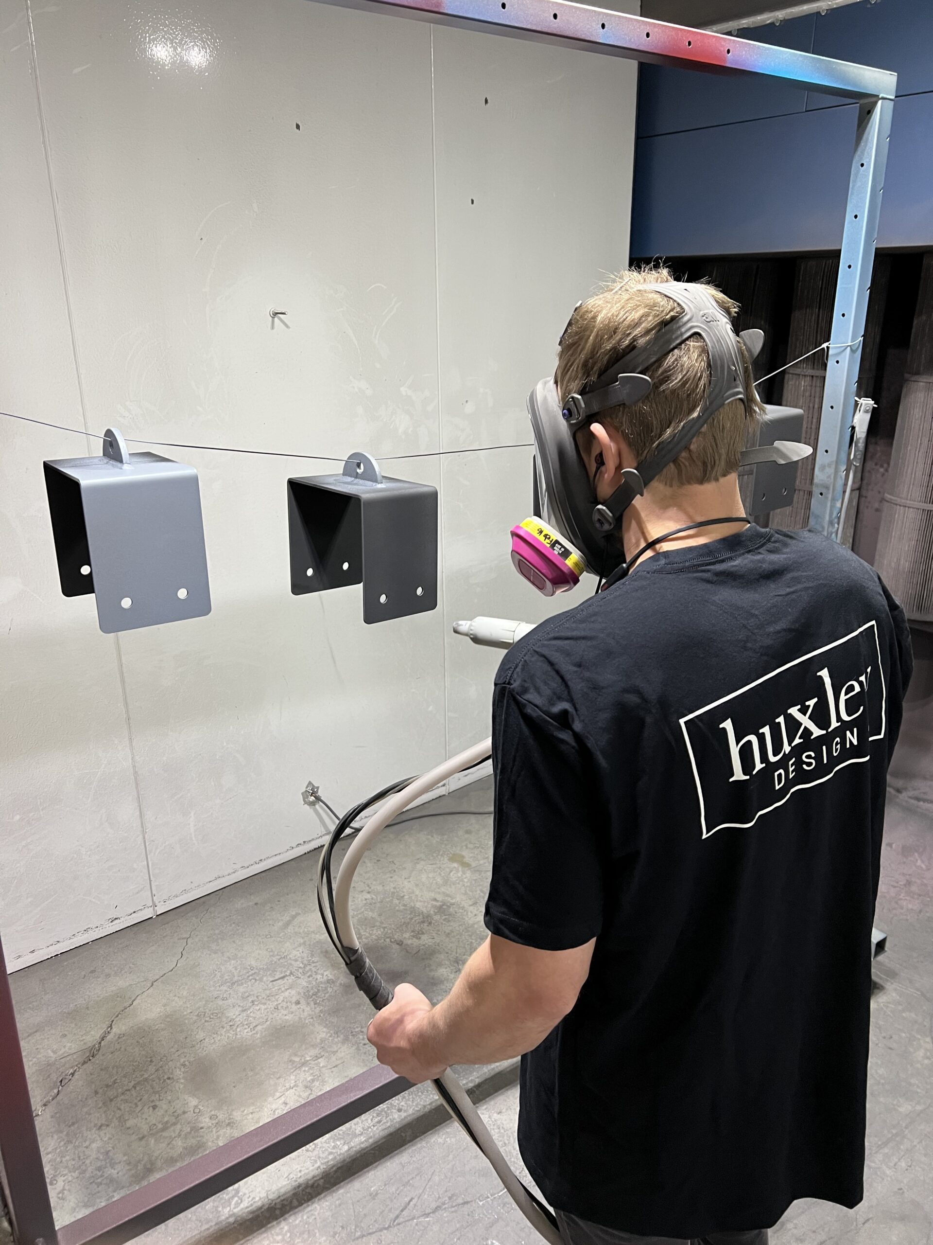 Huxley Design technician applying powder coating to metal parts with precision and care for a flawless finish.